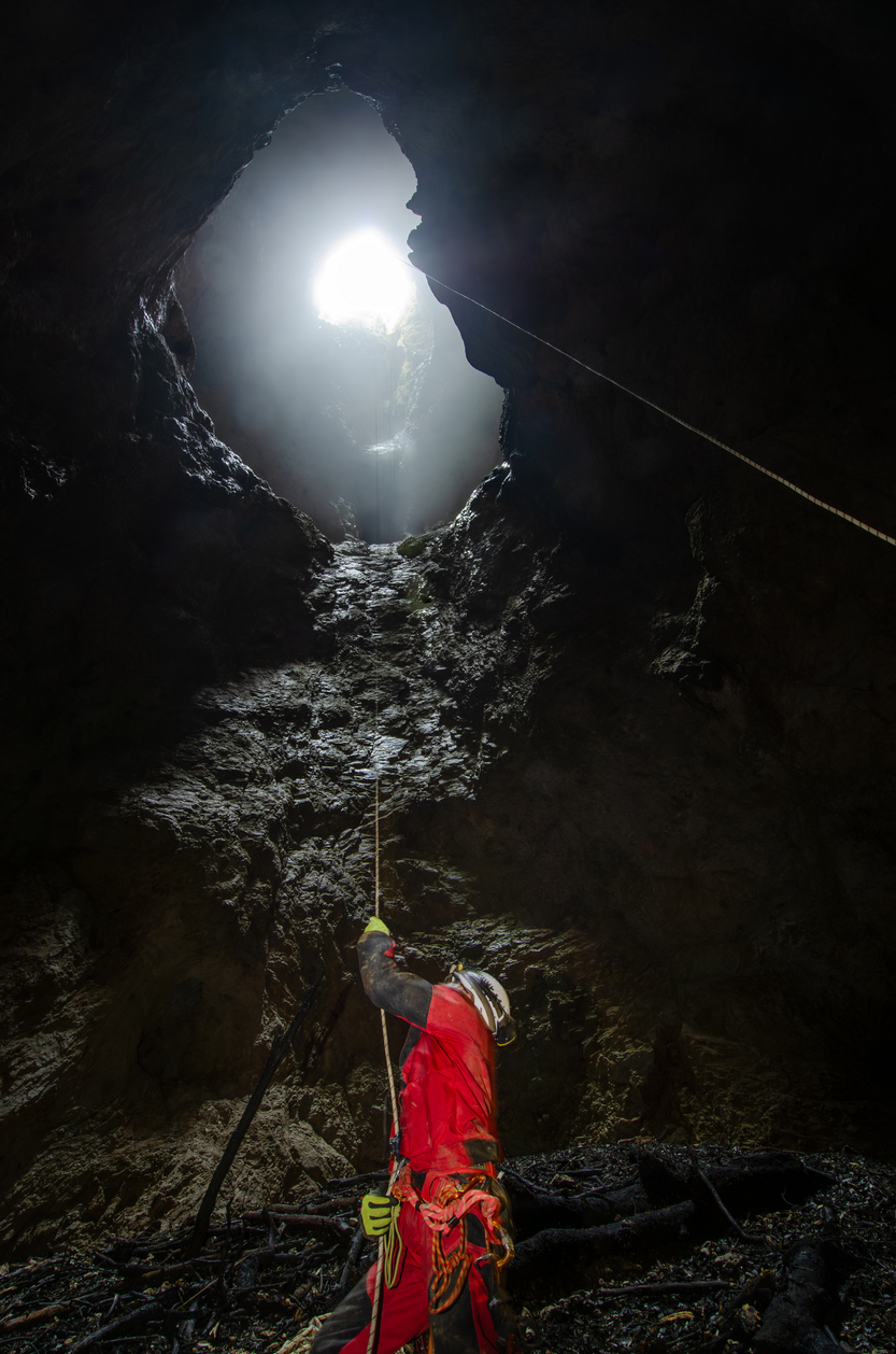Rescue worker in red gear climbing rope inside a cave during technical rescue training
