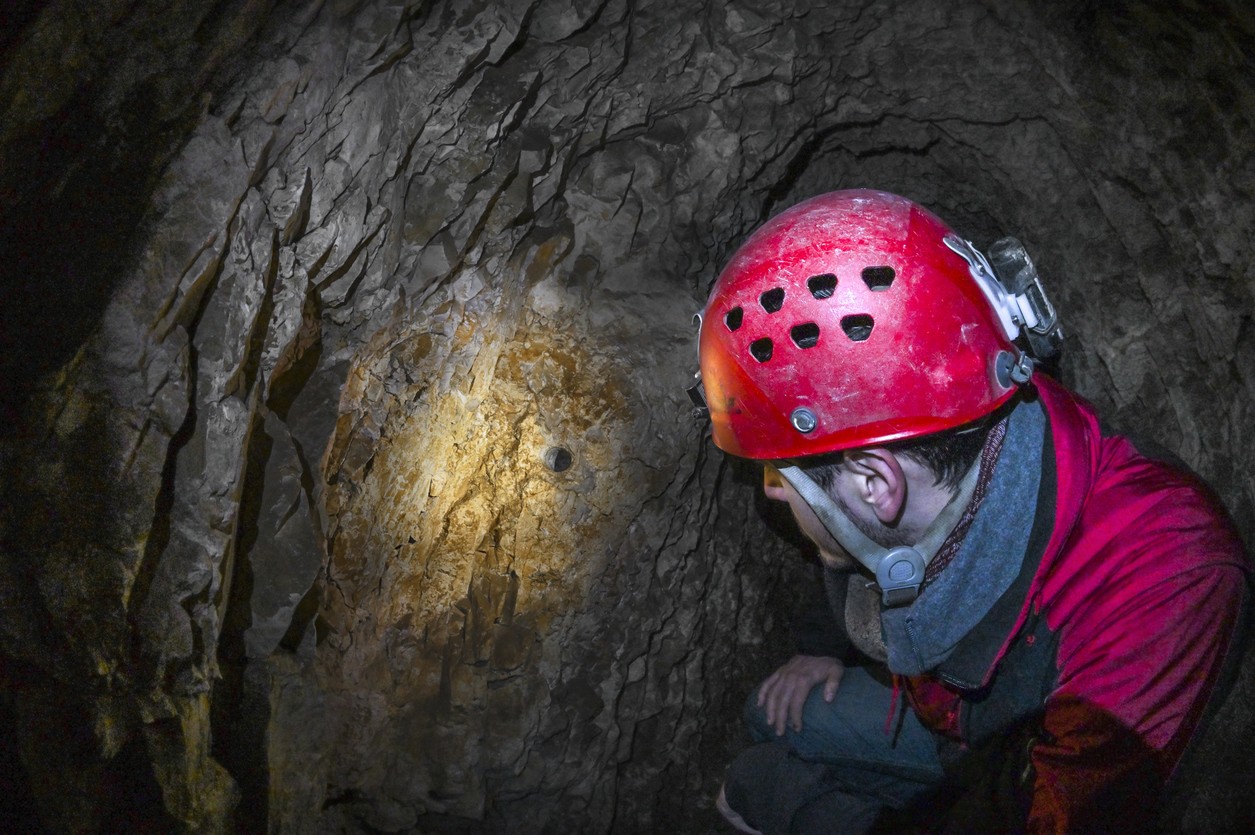Rescue worker in red helmet training inside a dark cave tunnel during technical rescue exercise
