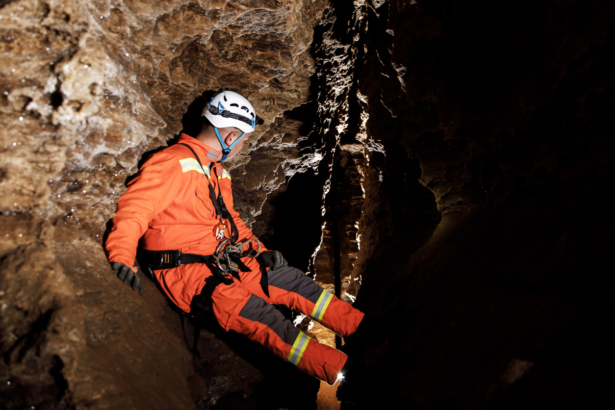 Rescue worker in orange suit and helmet training in a narrow cave passage
