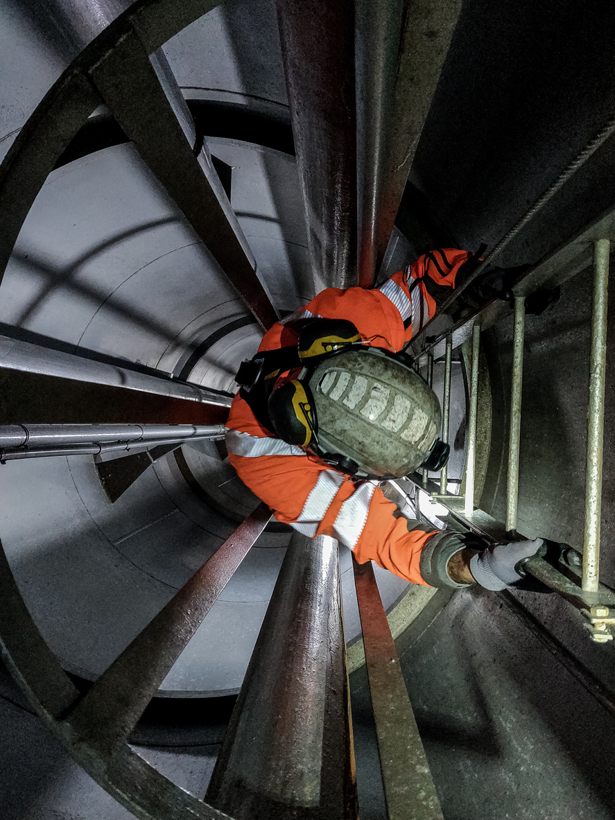 Rescue worker in safety gear climbing ladder inside industrial confined space