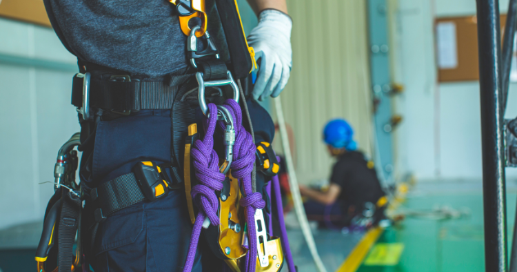 Rope rescue technician wearing a full-body harness with purple rescue rope and hardware attached, standing near a training area in the Greater Edmonton Area.