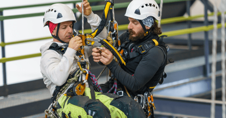 Two rescue technicians in helmets working together to adjust rope rescue equipment during a suspended training exercise.