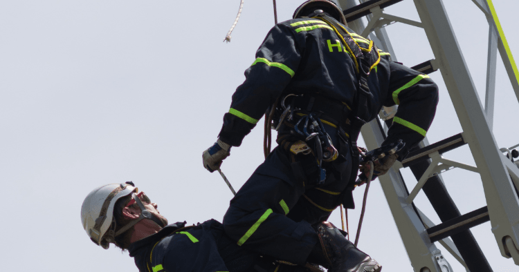Two rescue technicians in high-visibility gear performing a rope rescue at height on a tower structure.