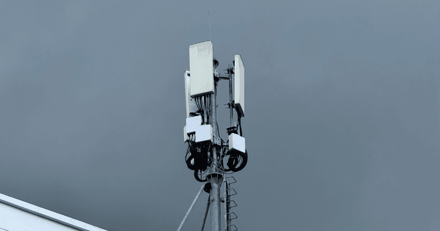 A small cell antenna array mounted on a pole against an overcast grey sky, with wiring and equipment boxes visible near the top.