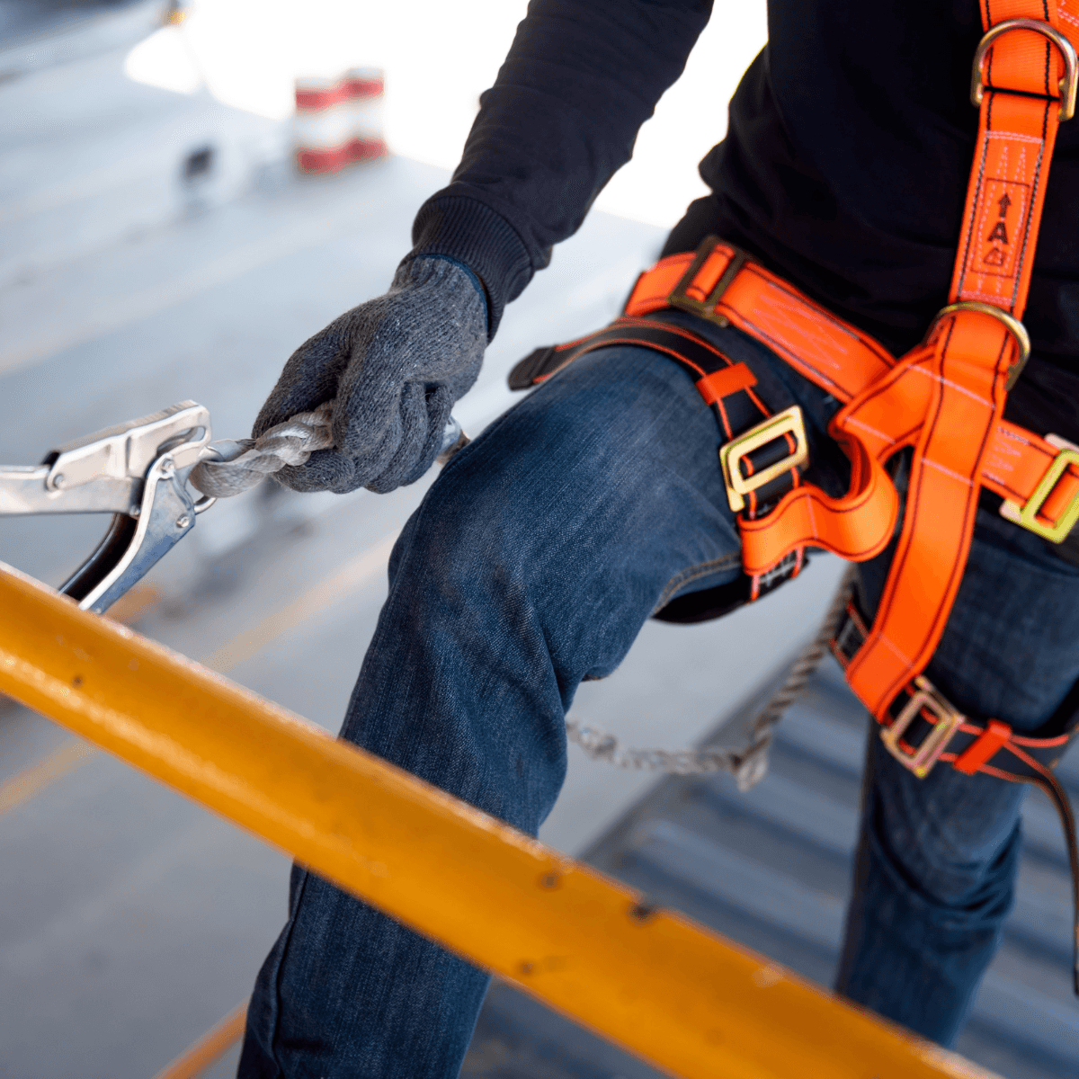 Close-up of a gloved hand securing a rope grab device to a lanyard near a yellow guardrail.