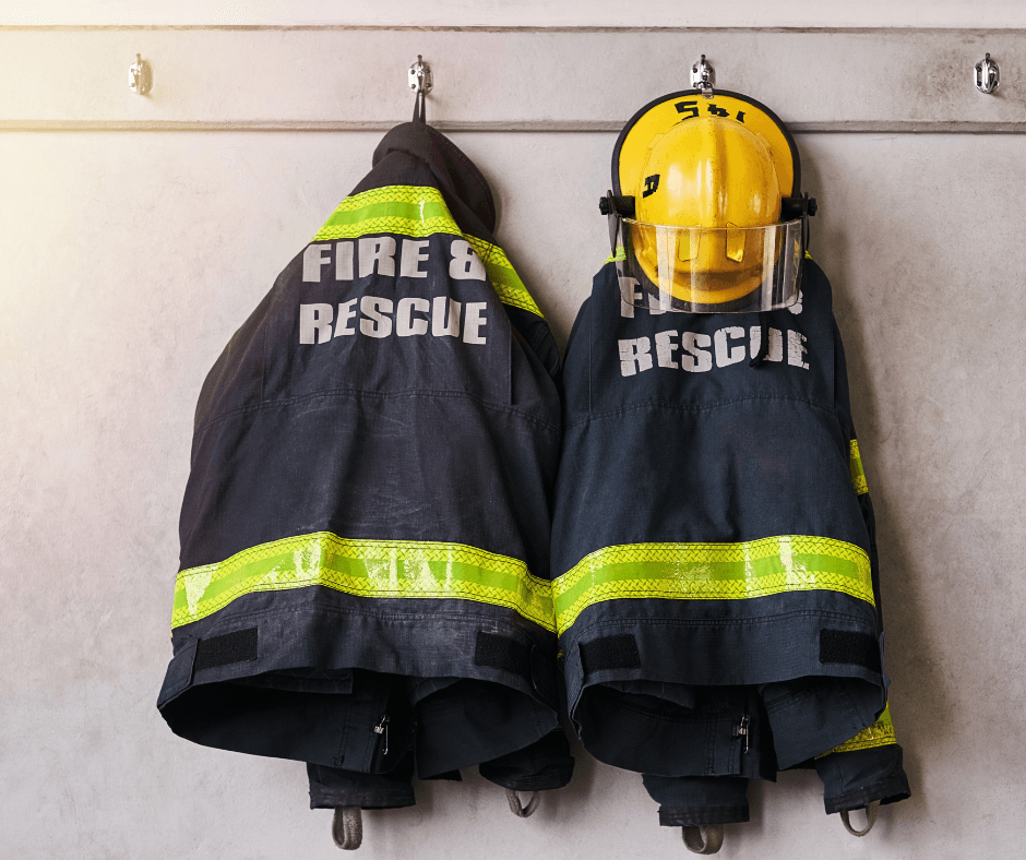 Two firefighter coats with reflective stripes and yellow helmet hanging on wall hooks in fire station